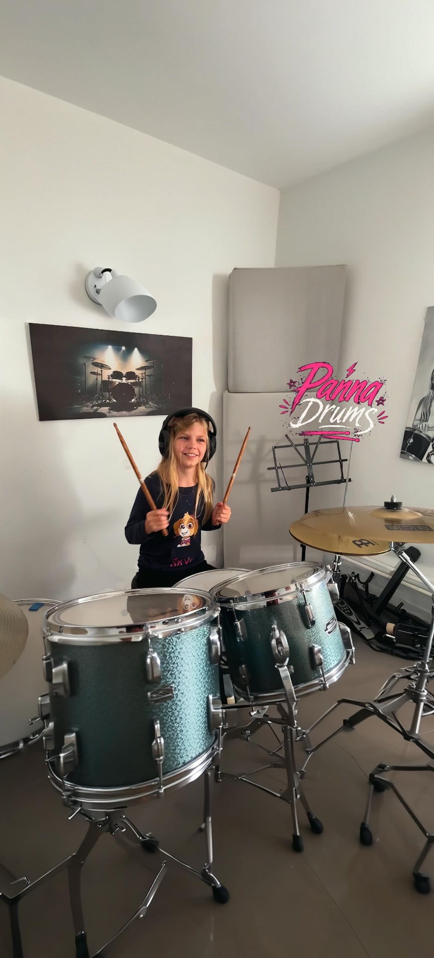 Panna fejhallgatóban a dobszettje mögött, mellette a Panna Drums logó a falon